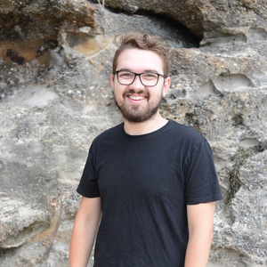 UNE student Cale Moloney standing by a rockface in a black tshirt and glasses