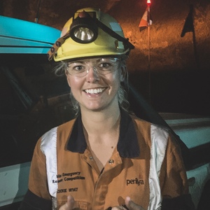 UNE graduate Jessie Cooke smiles in full mining gear and night headlamp