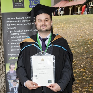 Bachelor of Economics with Honours graduate James Pryor poses with testamur at UNE graduation