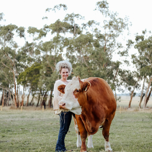 UNE Business graduate Ruby Canning stands in a field with a cow